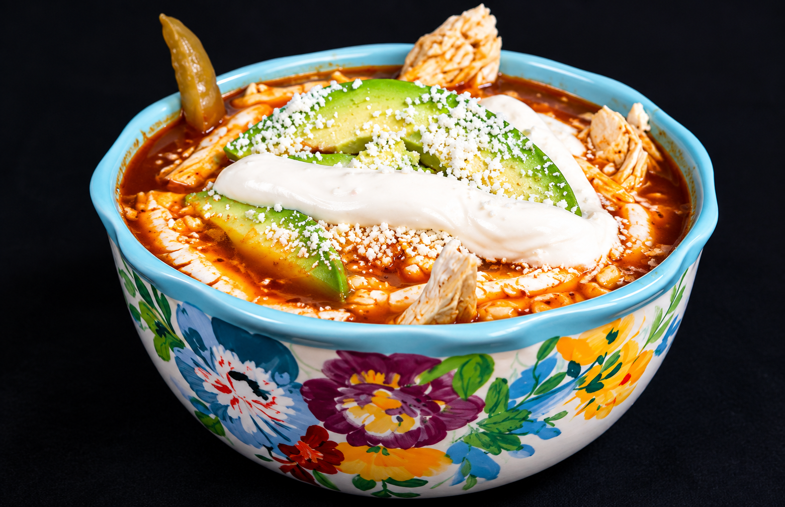Chicken tortilla soup topped with avocado, crema and cheese in a floral bowl
